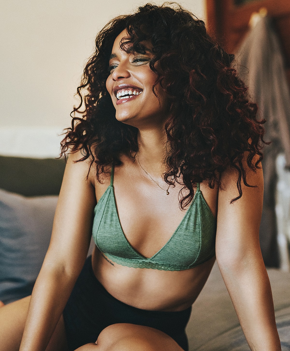 Smiling woman in green bralette, relaxed setting.