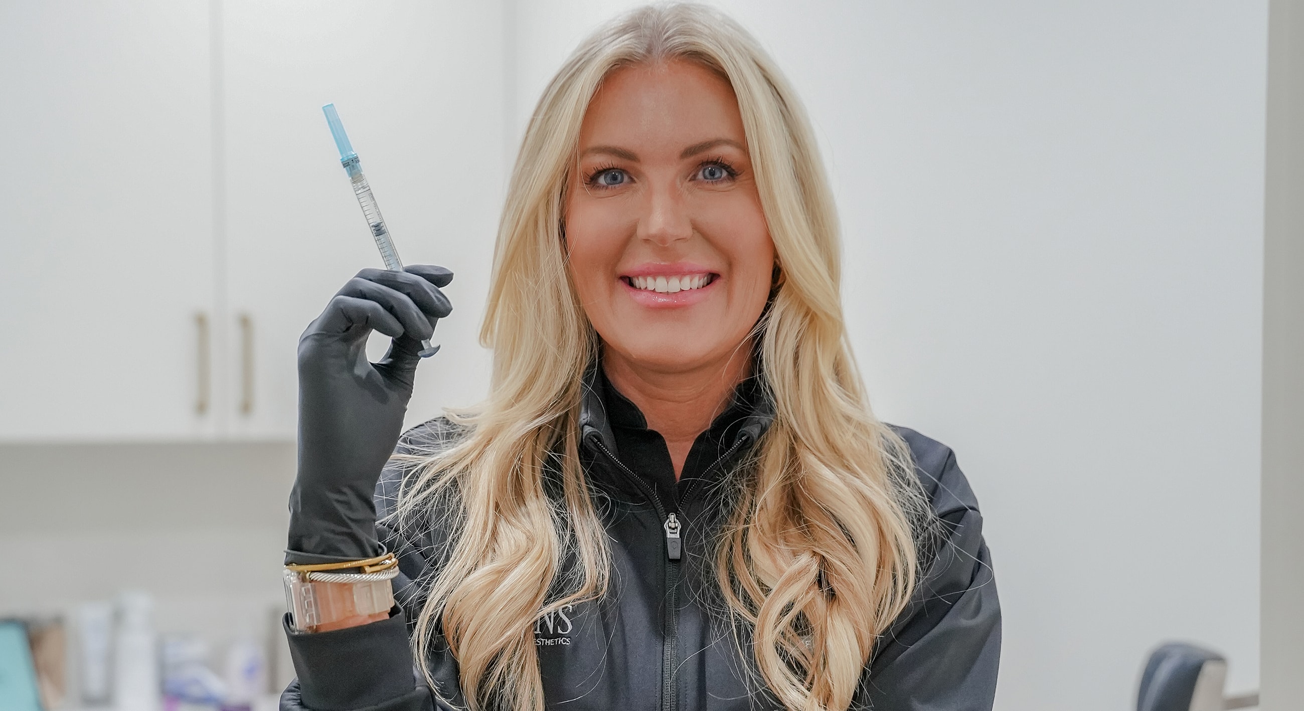Smiling woman holding a syringe in a clinic.