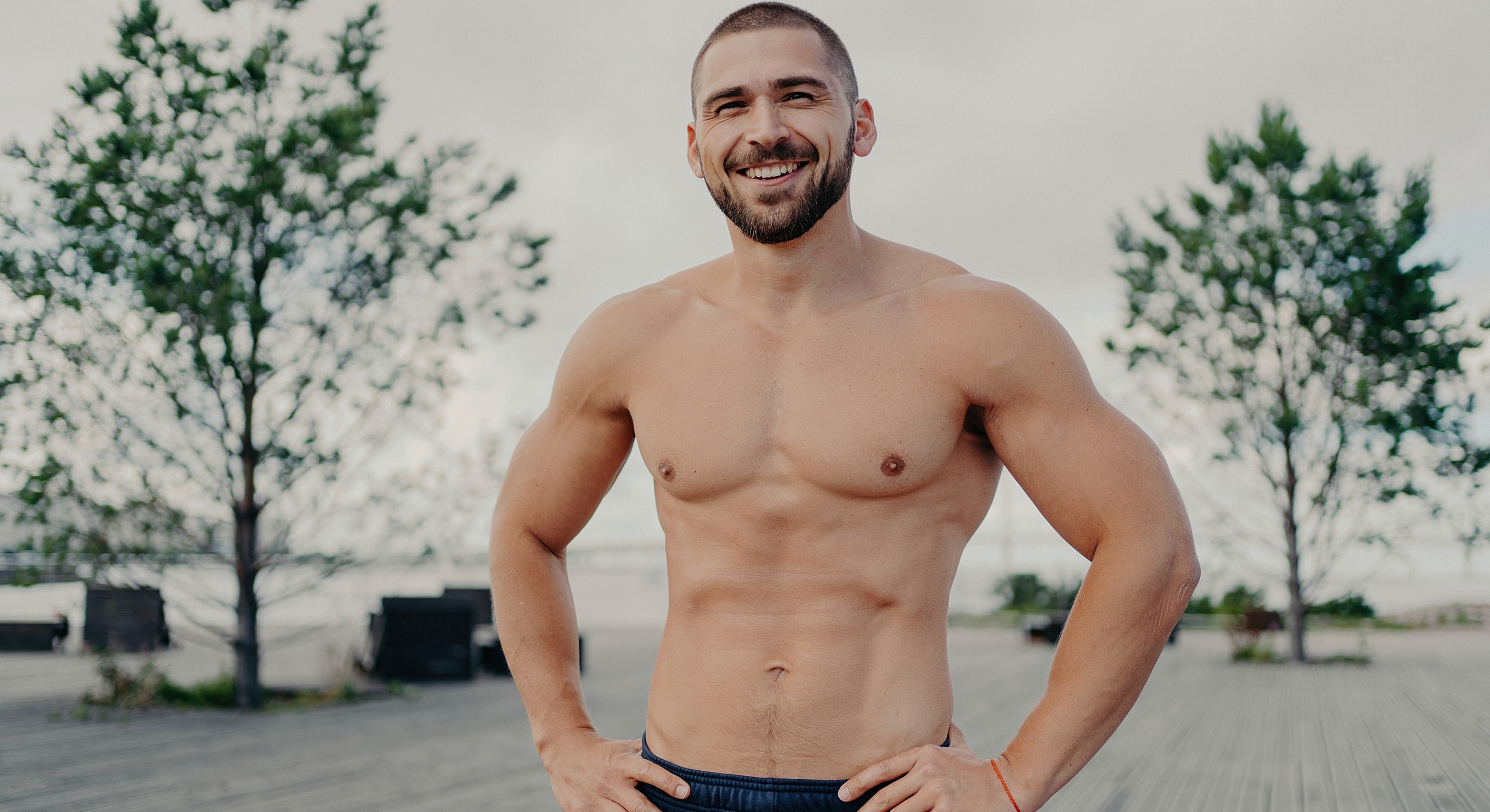 Man smiling outdoors, showcasing athletic physique.